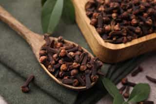 Dried cloves in a wooden spoon.